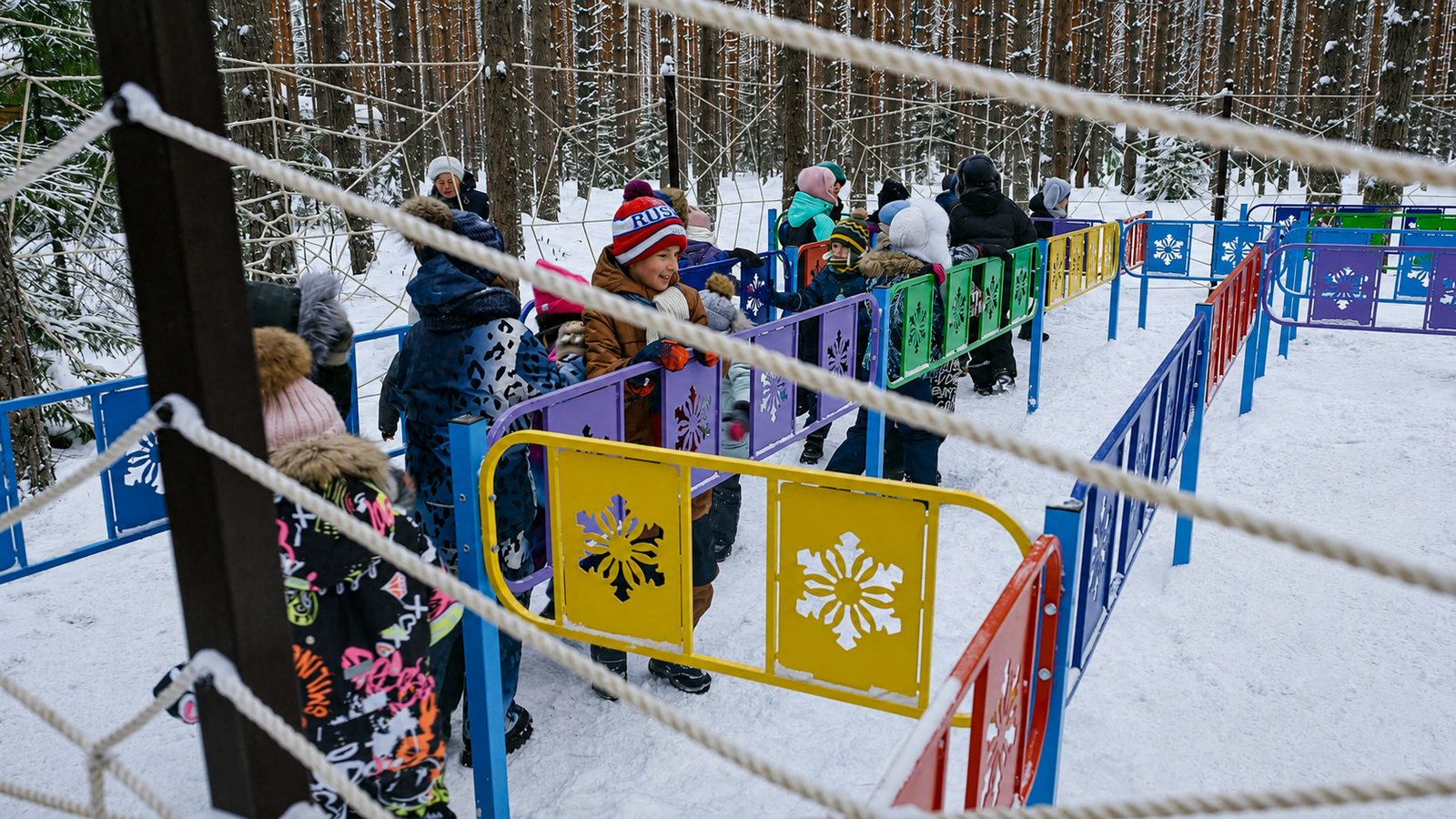 Дети проходят по яркому ограждённому мостку/полосе препятствий в заснеженном лесу.